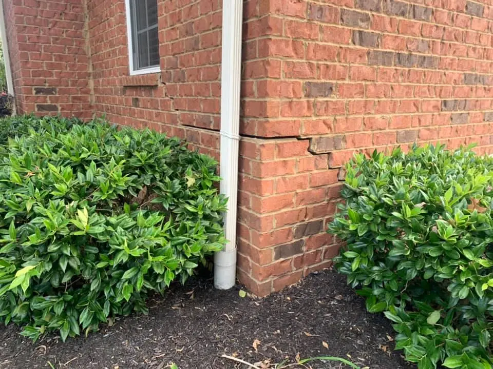 Ground Up Foundation Repair, Waterproofing and Concrete Leveling inspecting stair-step cracks in a brick foundation