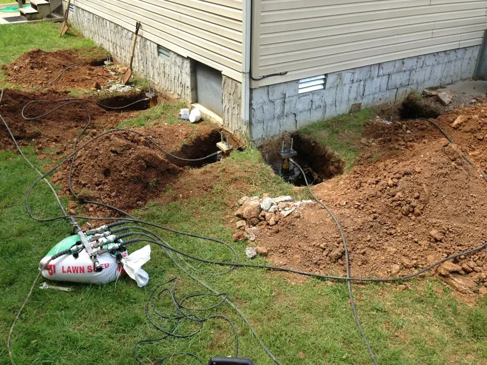 Ground Up Foundation Repair, Waterproofing and Concrete Leveling installing push piers with a hydraulic ram for foundation