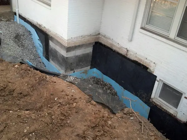 Installing an exterior waterproofing membrane and drainage around a foundation.