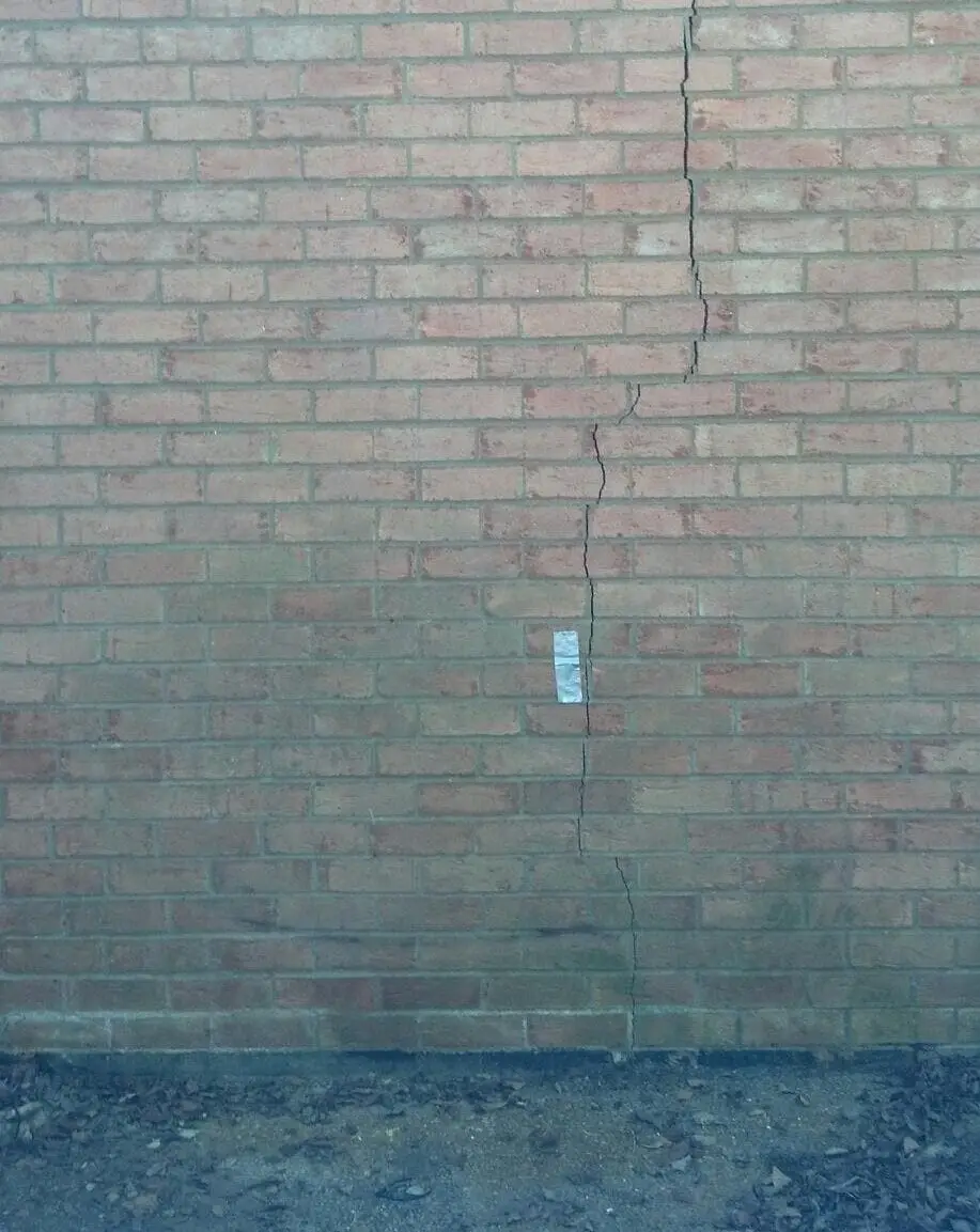 Ground Up Foundation Repair, Waterproofing and Concrete Leveling inspecting a vertical crack in an exterior brick foundation