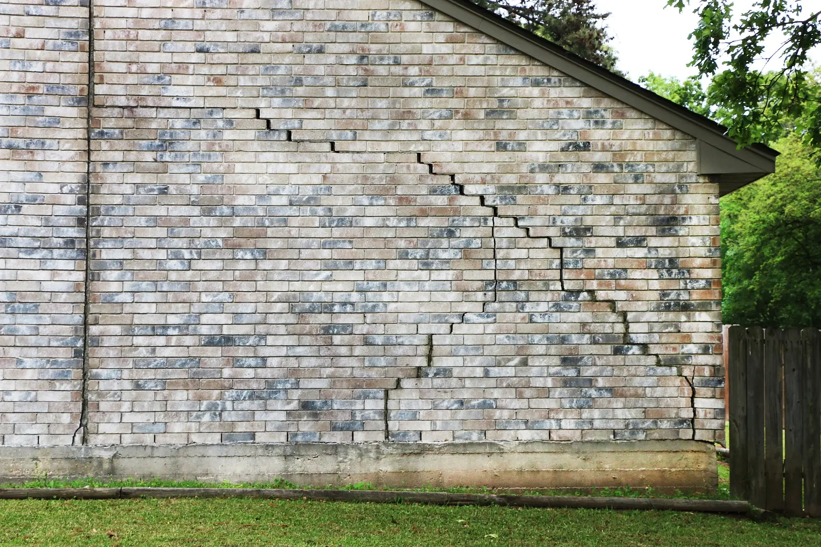 Ground Up Foundation Repair, Waterproofing and Concrete Leveling inspecting severe stair-step cracks in an exterior brick
