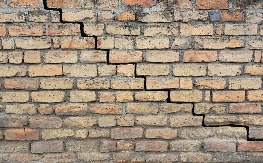 Ground Up Foundation Repair, Waterproofing and Concrete Leveling inspecting a stair-step crack in a brick foundation.
