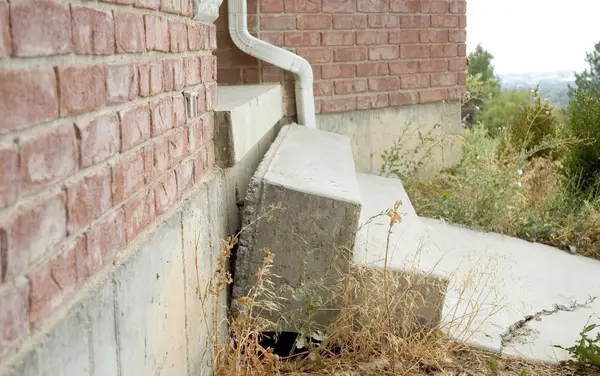 Ground Up Foundation Repair, Waterproofing and Concrete Leveling inspecting uneven concrete slabs and gaps next to a brick