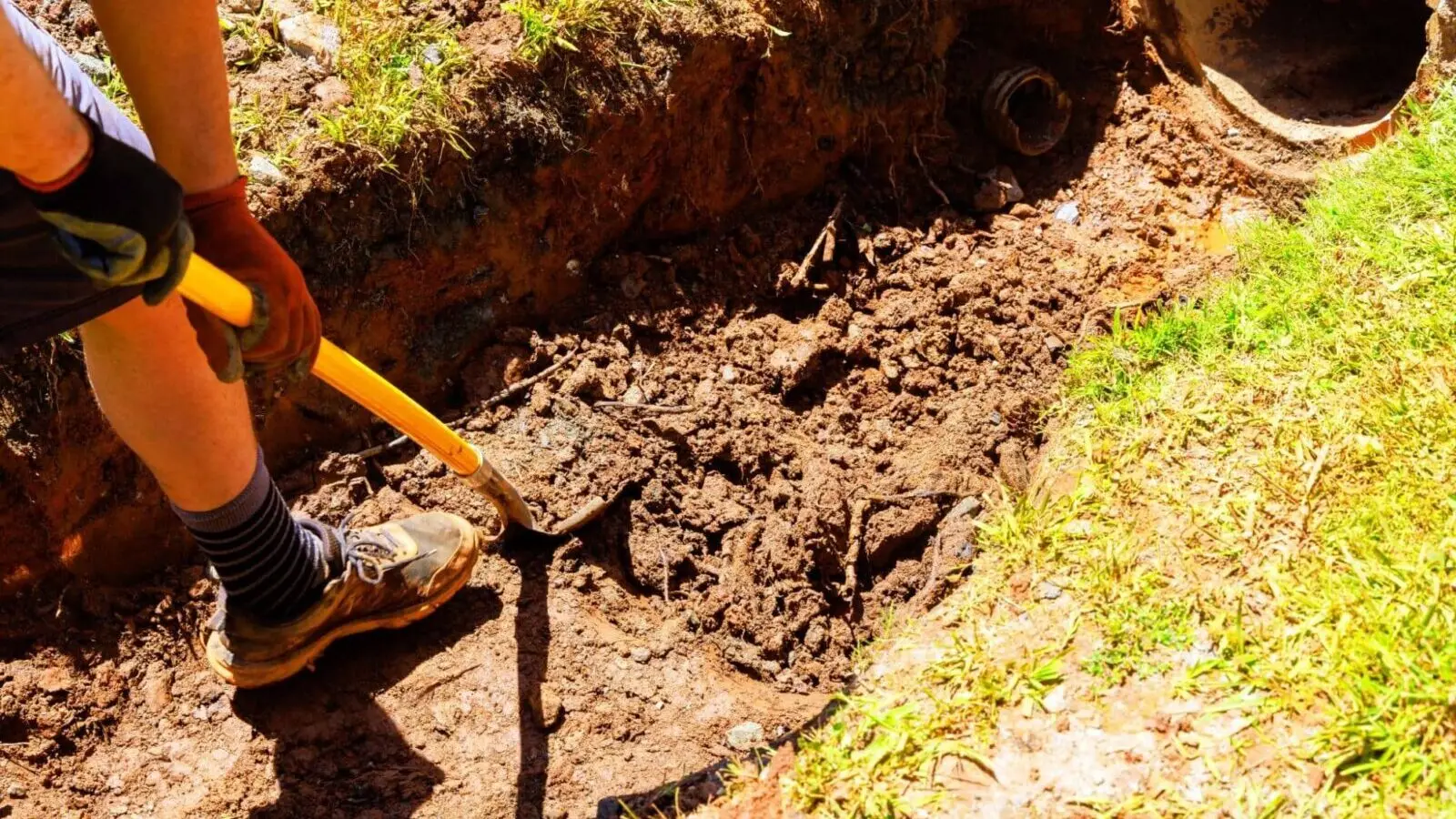 Ground Up Foundation Repair, Waterproofing and Concrete Leveling installing exterior French drain pipe in a newly dug trench.