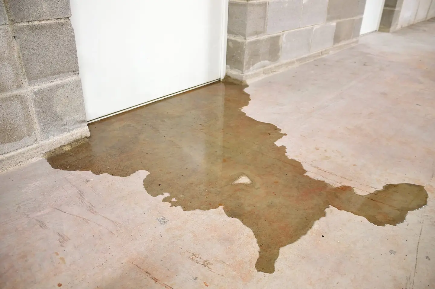 Ground Up Foundation Repair, Waterproofing and Concrete Leveling inspecting pooled water on a basement floor.
