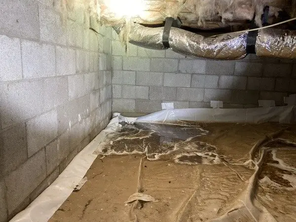 Waterproofing work along a block foundation wall in a wet crawl space.