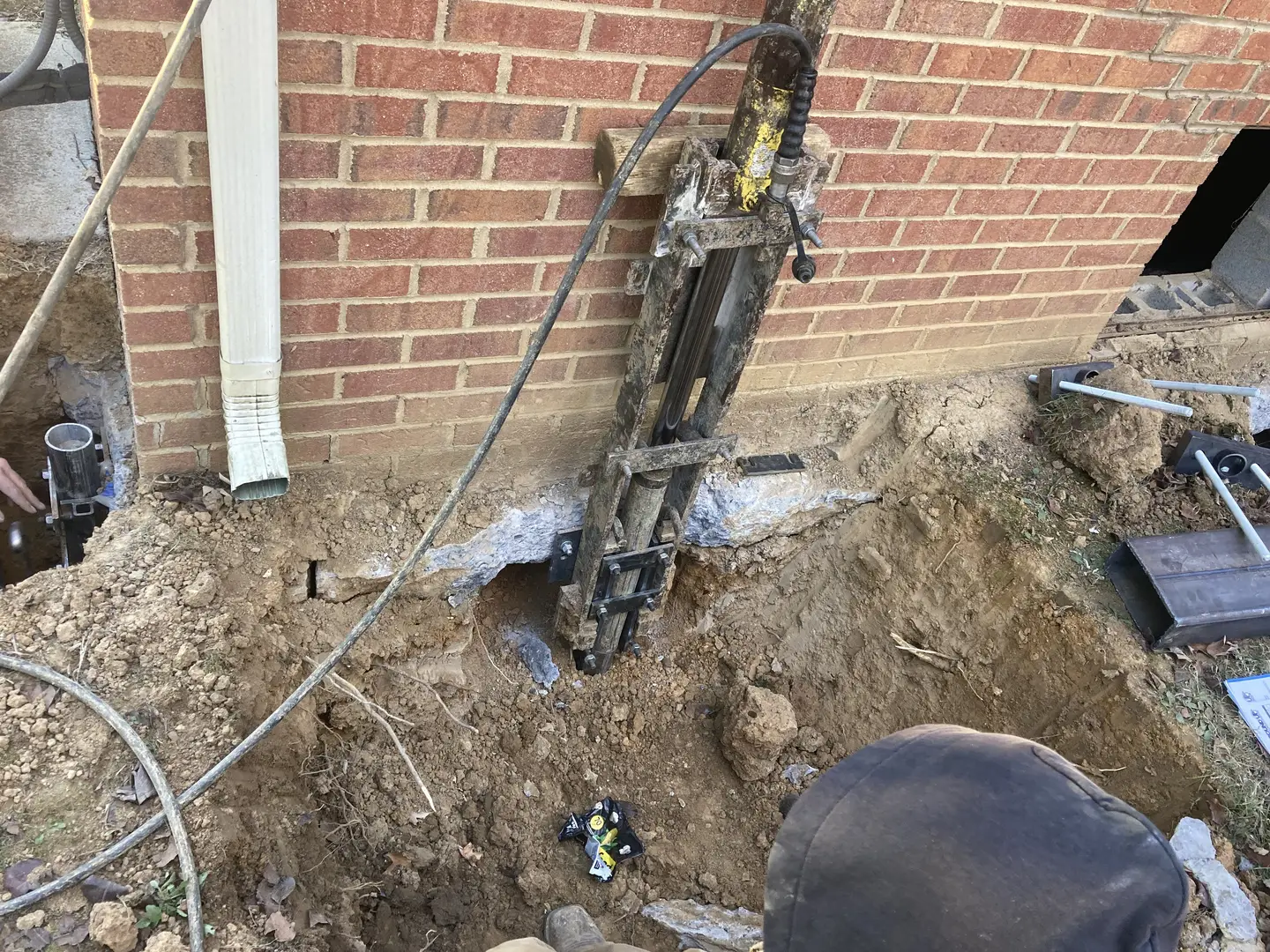 Ground Up Foundation Repair, Waterproofing and Concrete Leveling installing push piers with a hydraulic ram at an exterior